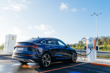 Audi e-tron charges under sunny sky.