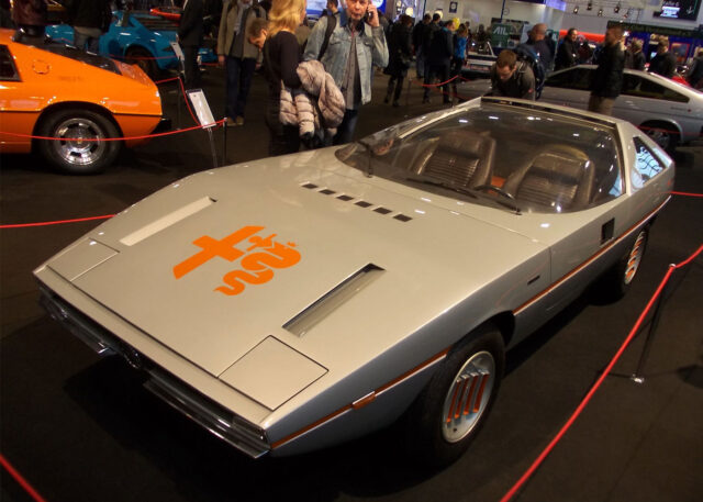 Futuristic silver concept car with orange emblem showcased.