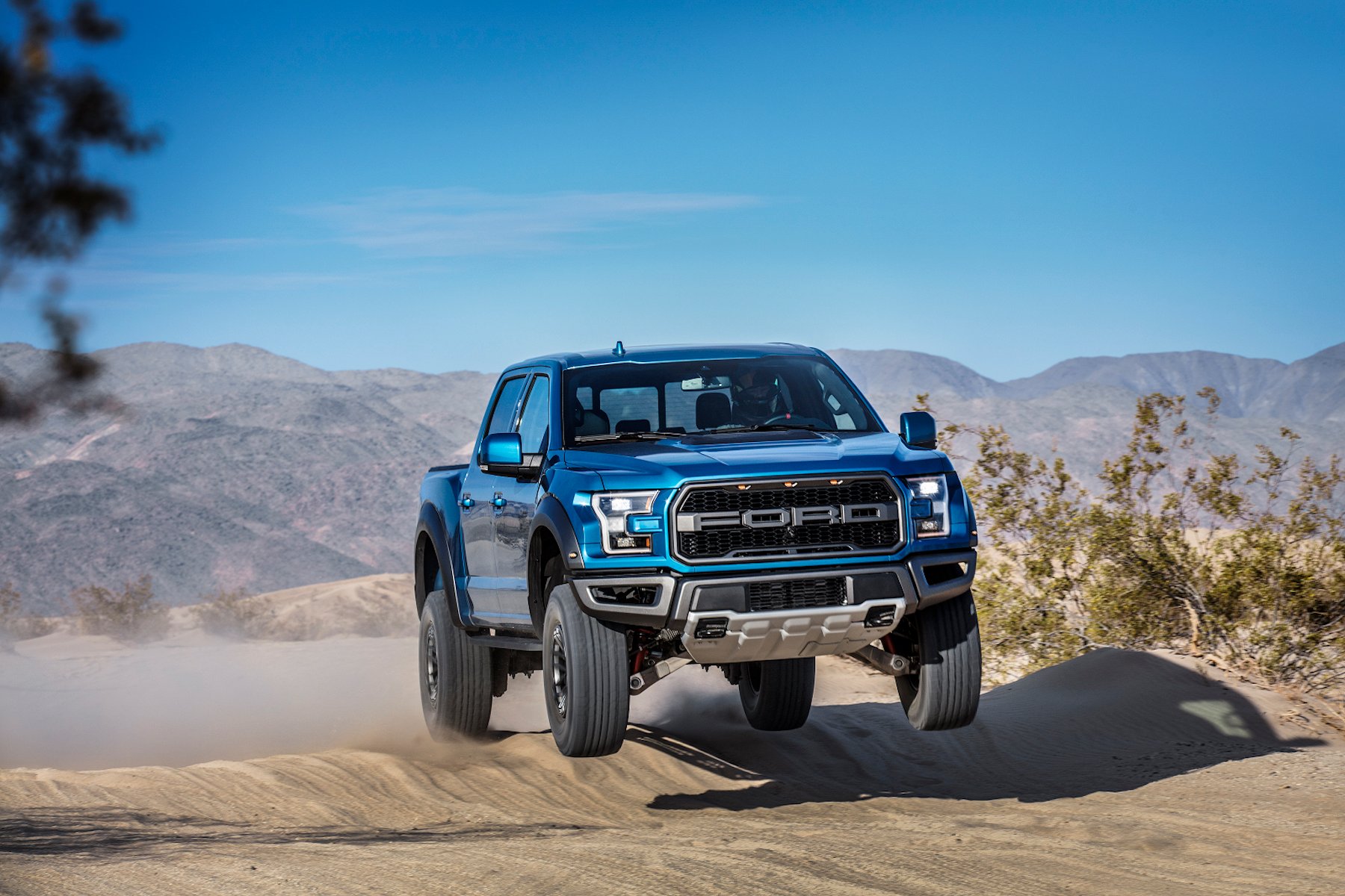 A blue pickup truck jumps desert hill.
