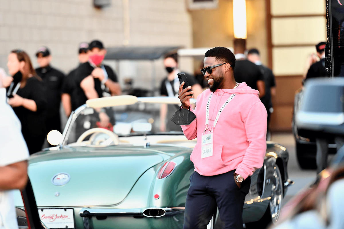 Person in pink hoodie smiles near classic Corvette.