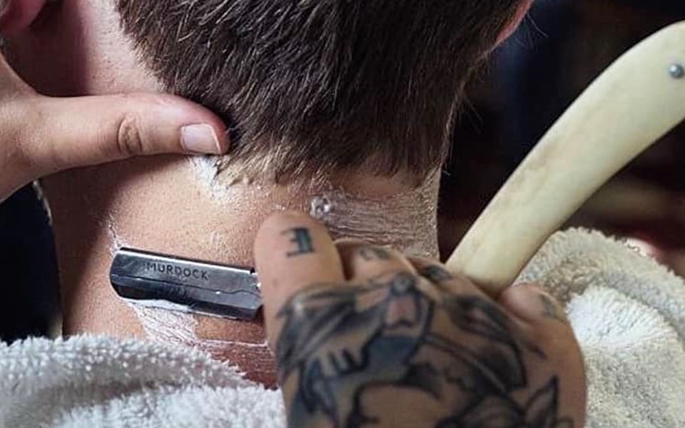 Tattooed barber's precise straight-edge shave.