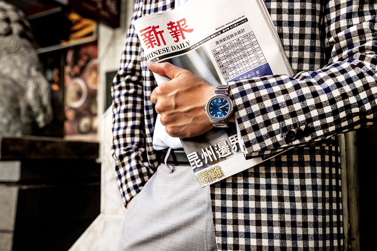Person in checkered blazer with Piaget Polo Watch and "Chinese Daily" newspaper, festive Lunar New Year decor behind.