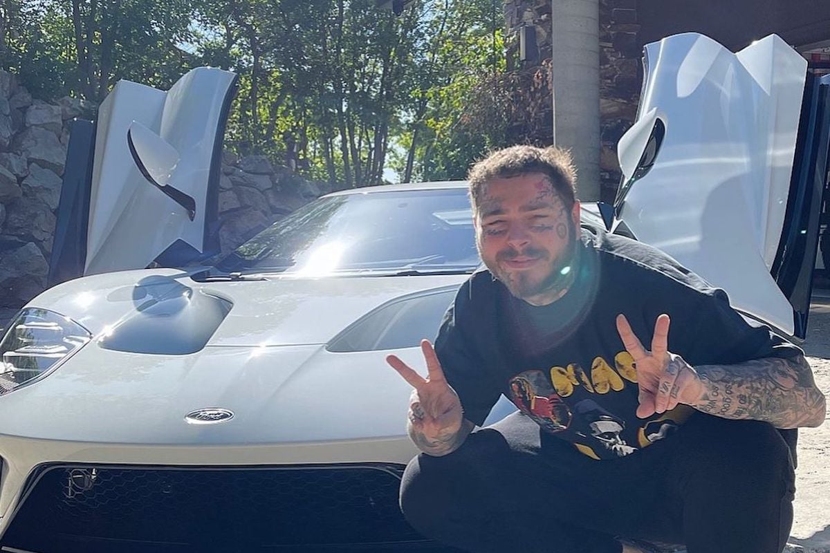 Man poses by supercar, peace sign up.