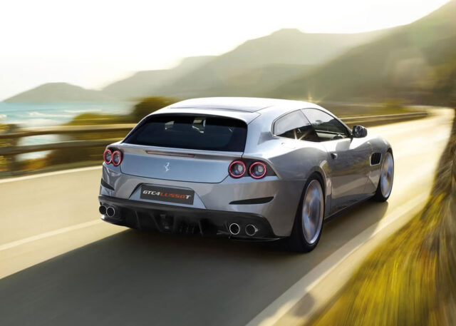 Silver sports car speeds along coastal road.