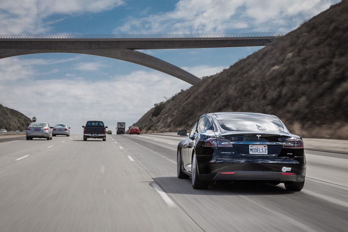 A black Tesla drives on a highway.