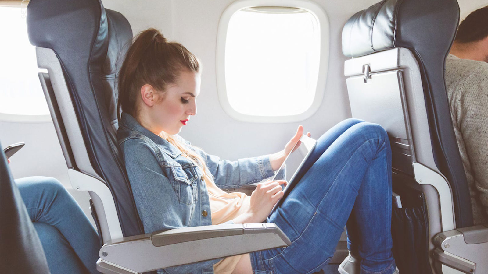 Person in denim, uses tablet on flight.